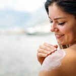 Attractive woman with healthy skin applying sunscreen to shoulder on summer vacation at beach
